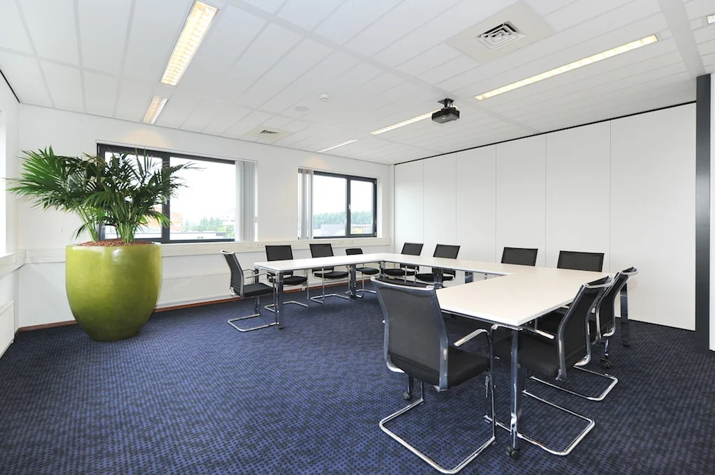 Moderne vergaderruimte aan de Laan van S-Gravenmade met U-vormige tafelopstelling, zwarte stoelen en grote groene plant.